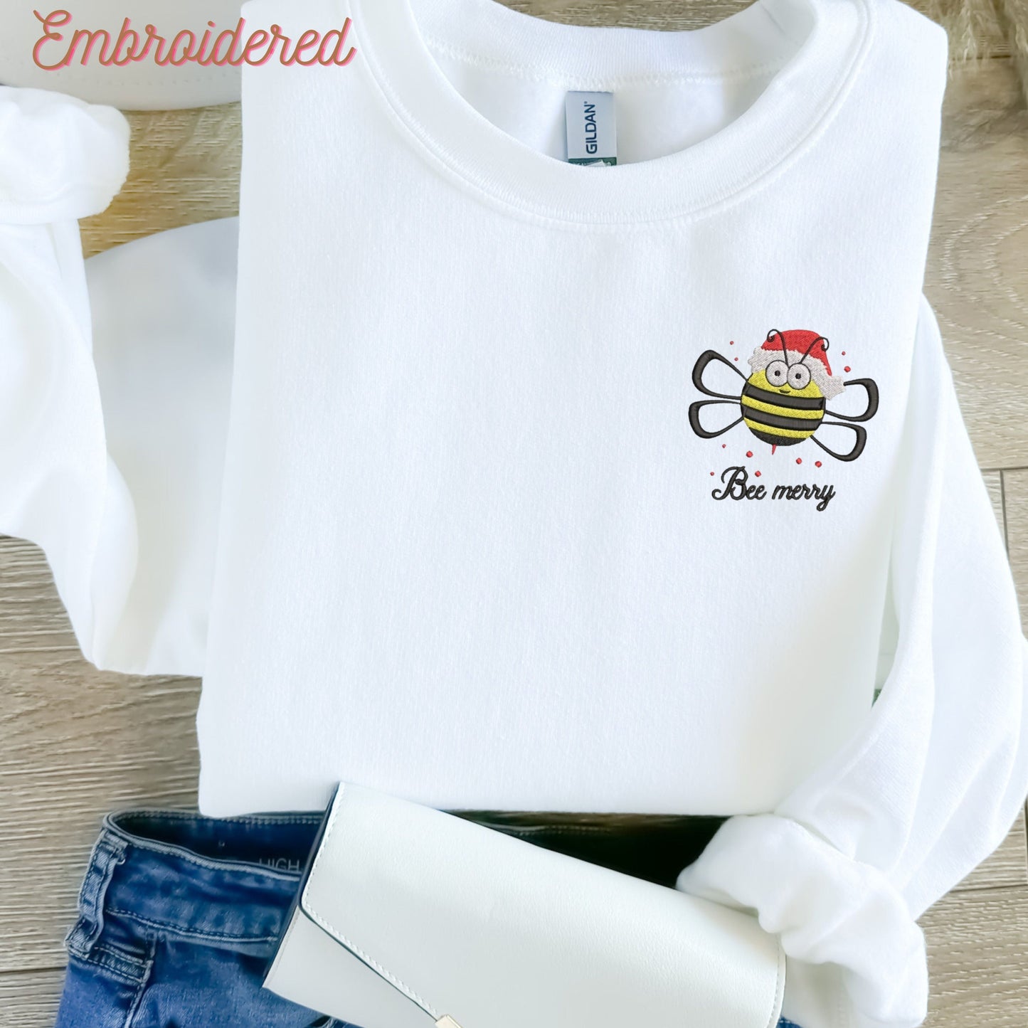 White crewneck fleece lined sweatshirt with a bee with a Christmas hat embroidered on the left chest area.