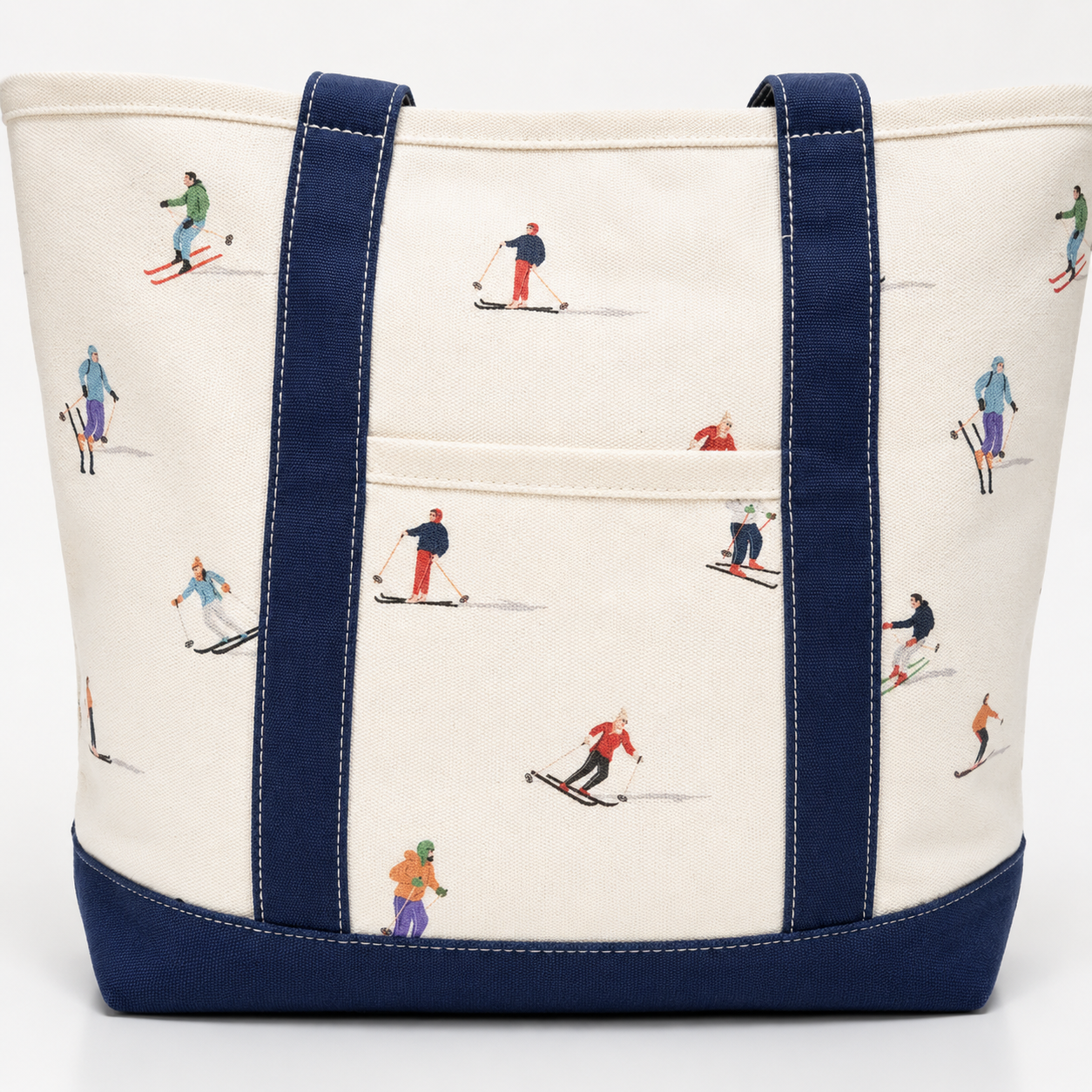 An off-white canvas tote bag with navy blue straps, bottom trim, and a front pocket, decorated with a repeating pattern of skiers and snowboarders in various colorful outfits.