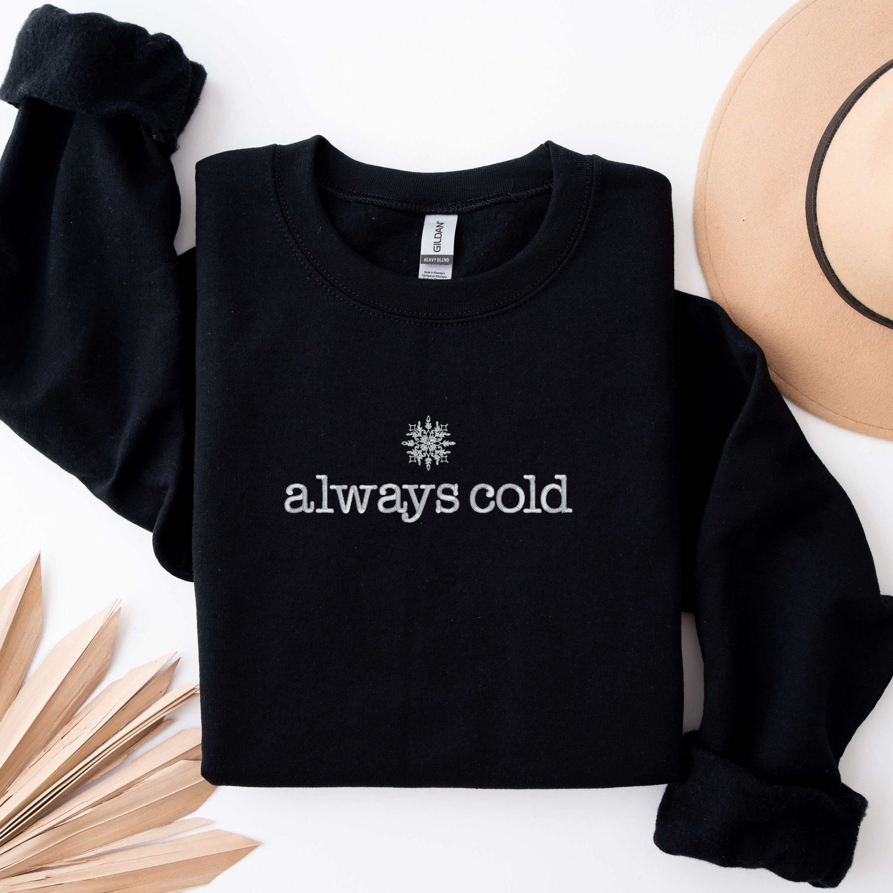 Navy crewneck sweatshirt with &quot;always cold&quot; embroidered onto the front of the sweater.
