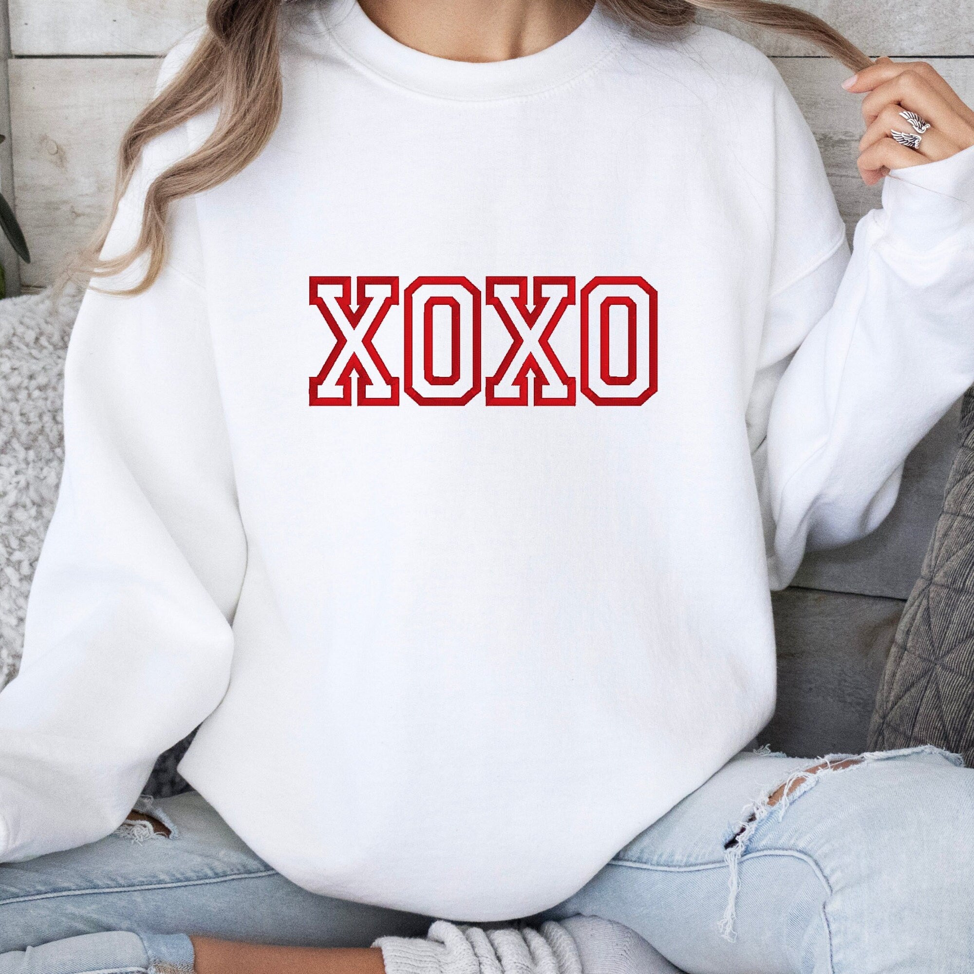 A white crewneck sweatshirt with XOXO embroidered on the front.