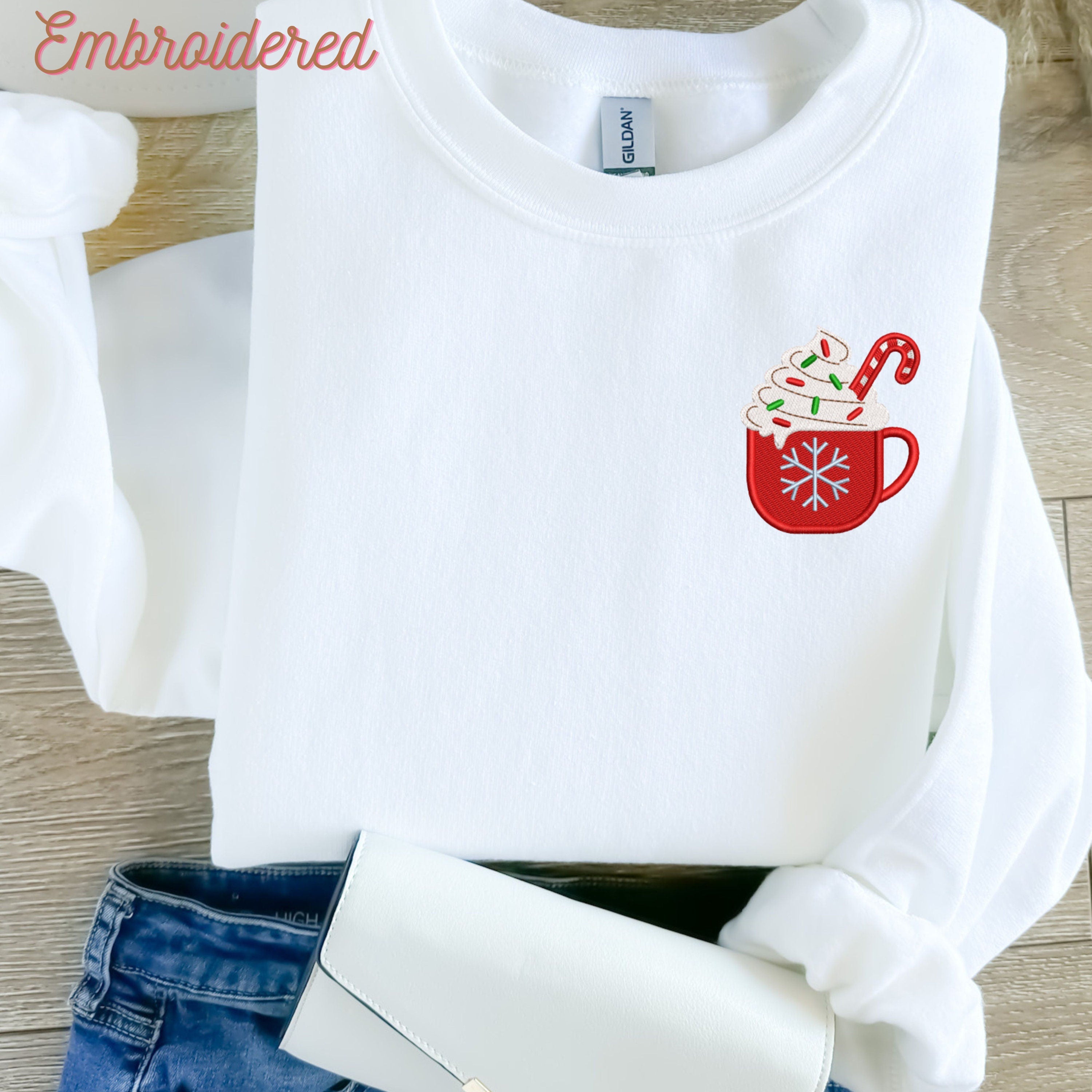 White crewneck fleece lined sweater with a cup of Christmas embroidered on the left chest.