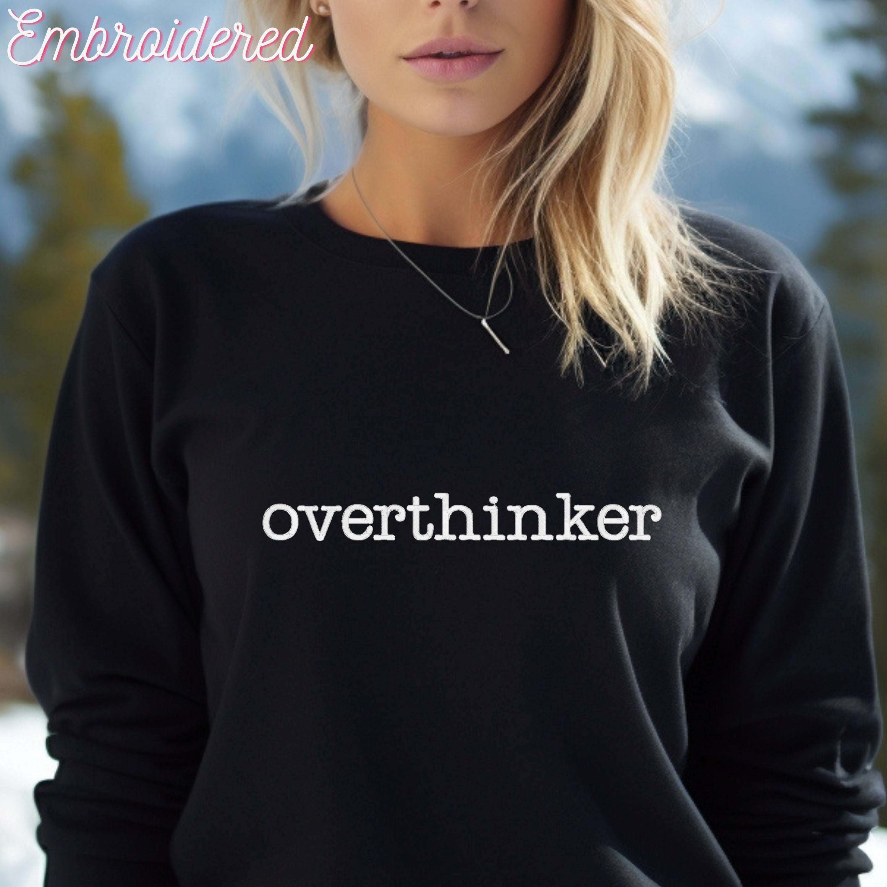 Overthinker embroidered in white thread onto a black crewneck sweater, chest area.