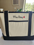 Beige Canvas Tote embroidered with Teachers name with a red apple next to it.